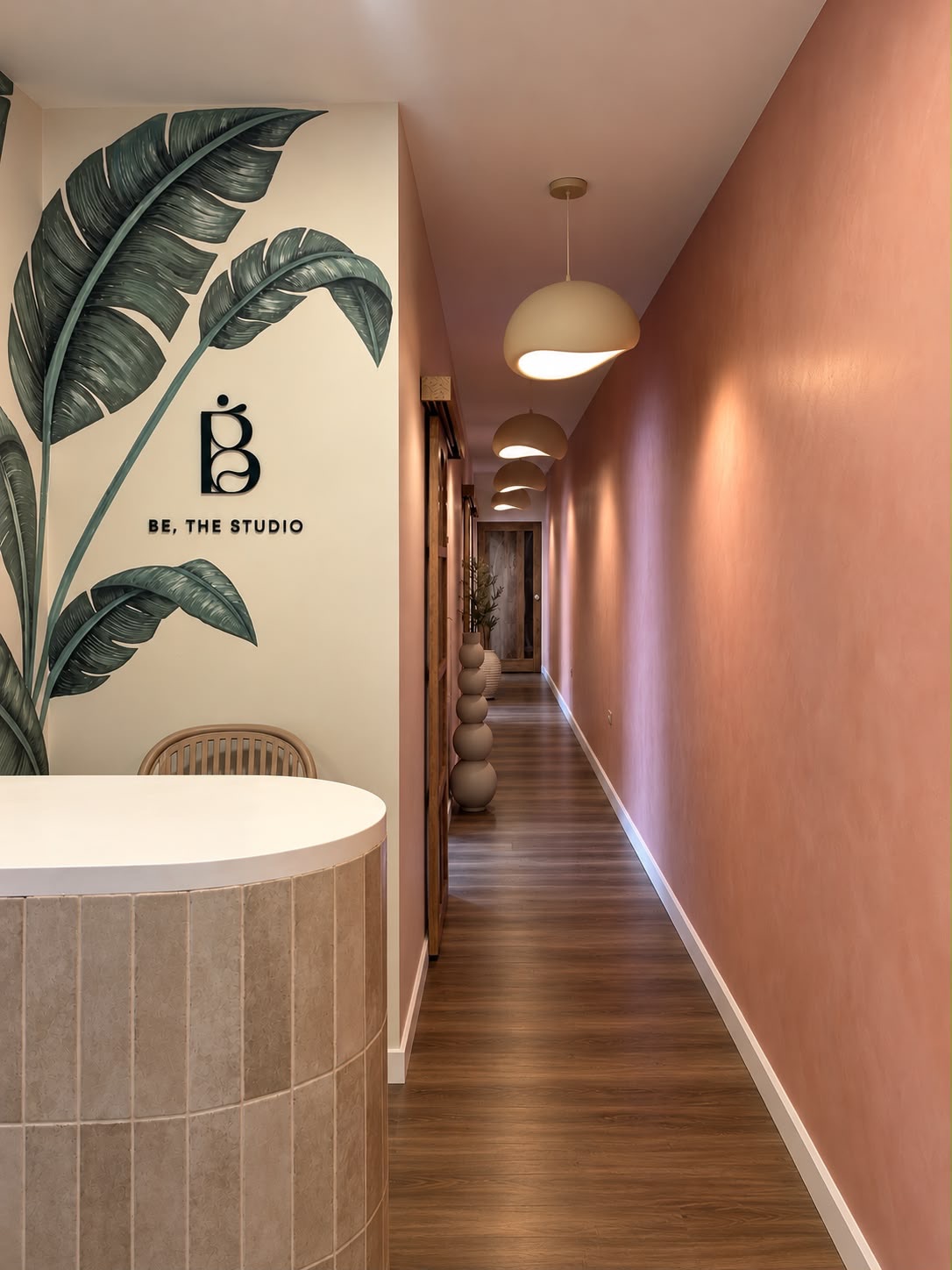 The entrance at Be. The Studio: the reception desk, a palm leaf mural with the studio logo, and the warm pink hallway to the studio rooms